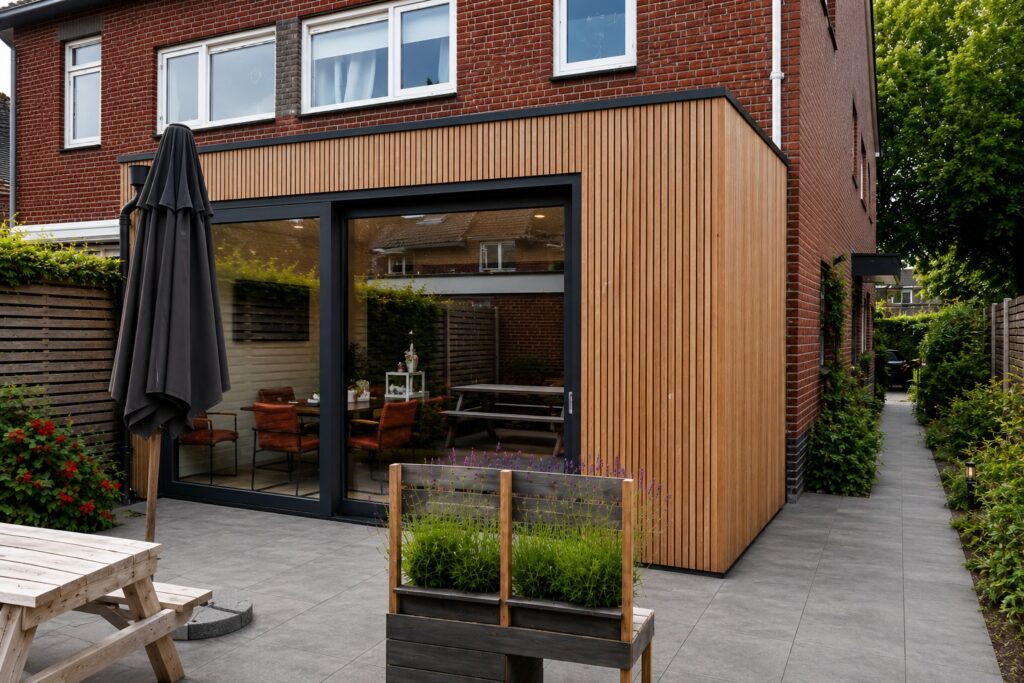 Moderne uitbouw in Austerlitz met houten gevelbekleding, zwarte kozijnen en grote glazen schuifpui