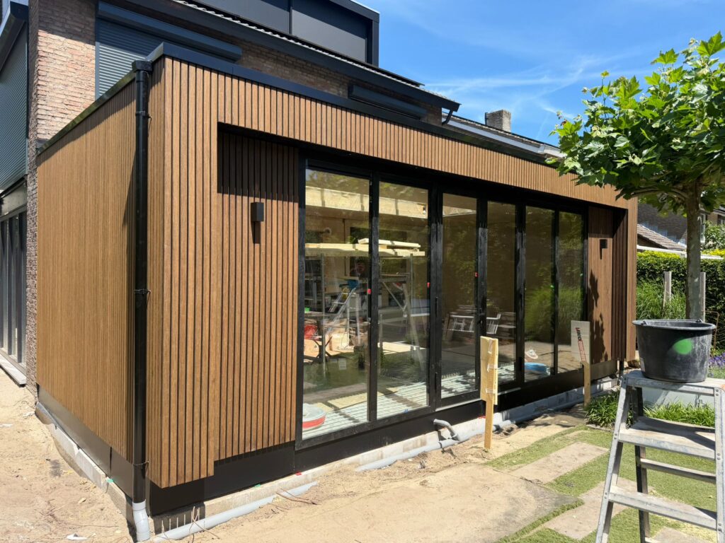 Moderne woninguitbouw in Amsterdam met houten gevelbekleding, zwarte kozijnen en grote glaspartijen