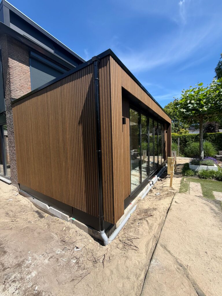 Zijaanzicht van een moderne uitbouw in Amsterdam met verticale houten gevelbekleding en zwarte dakrand