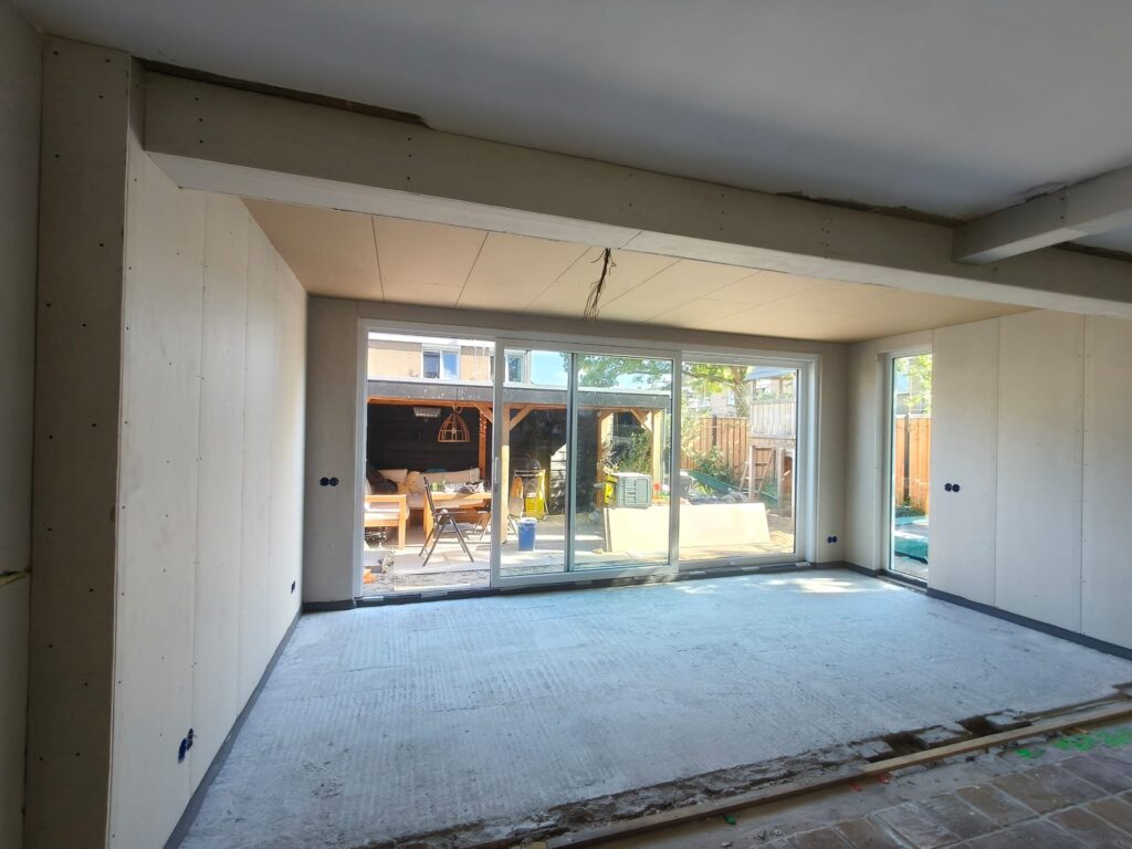 Binnenzijde van een ruime woninguitbouw met grote glazen schuifpui en zijraam